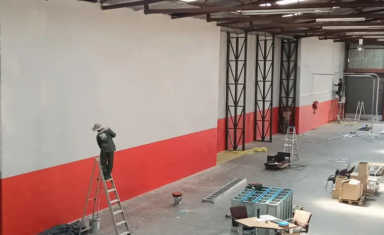 Worker on a ladder painting a warehouse interior with a red band