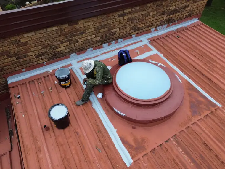 Worker kneeling on a freshly coated red metal roof beside open tins